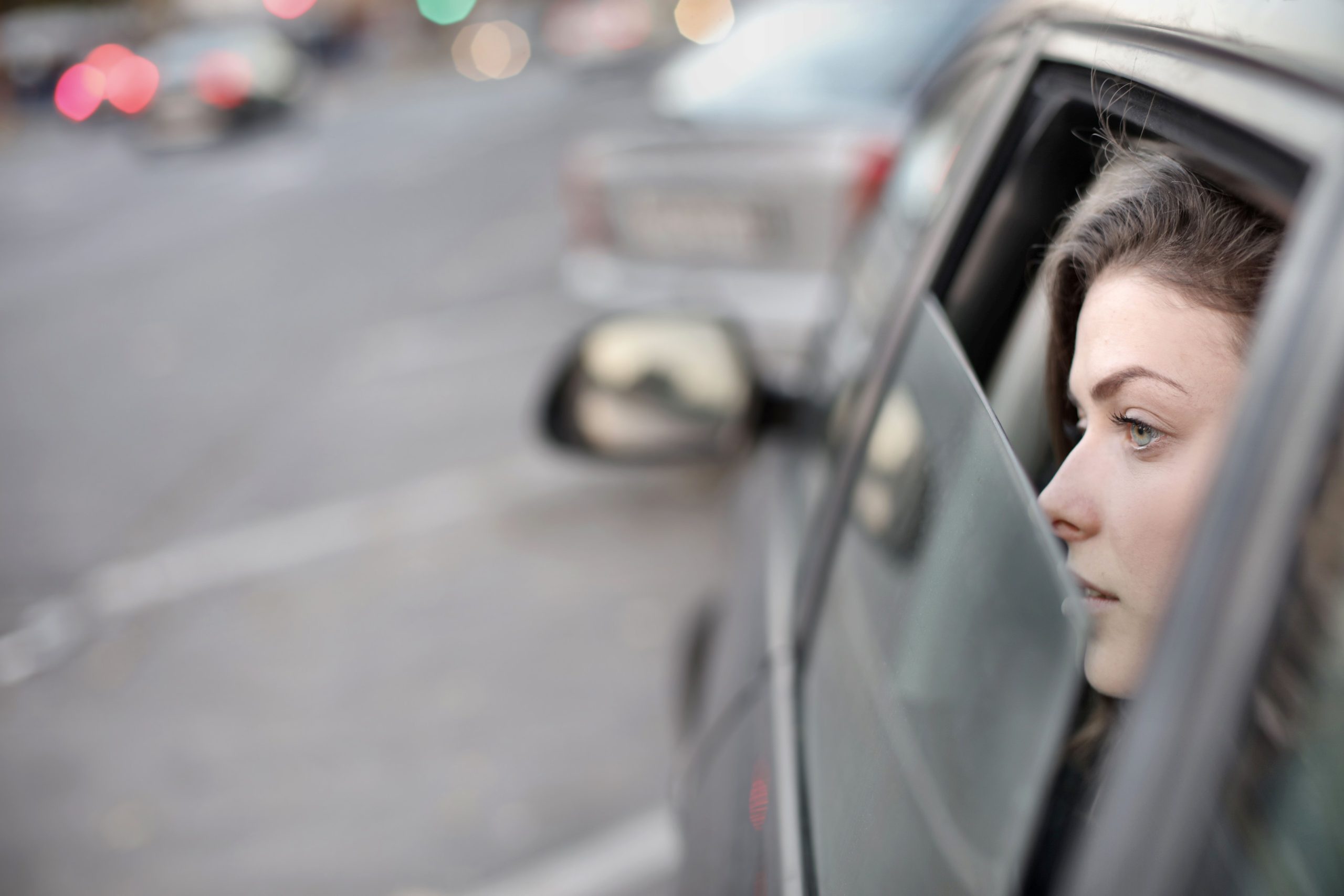 A woman gazes out the window of a car on a bustling city street, reflecting travel and contemplation.